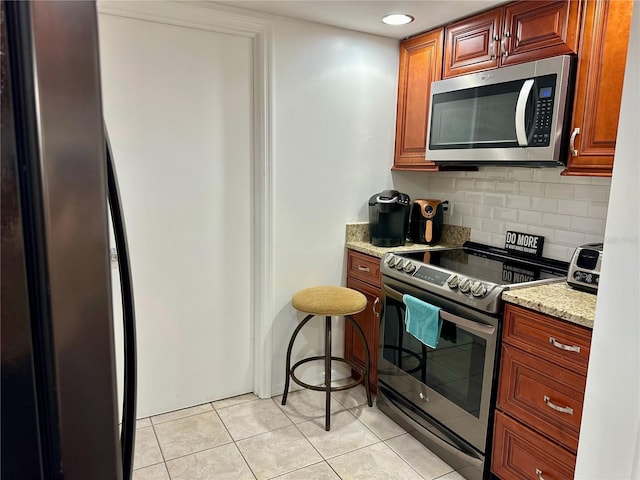 kitchen featuring decorative backsplash, light tile patterned flooring, light stone countertops, and stainless steel appliances