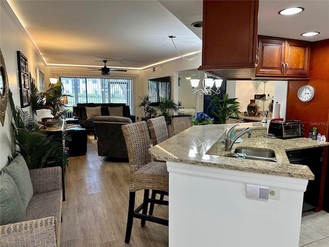 kitchen with dishwasher, ceiling fan with notable chandelier, sink, light stone countertops, and a kitchen bar