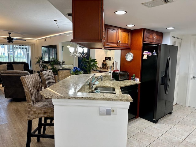 kitchen with light stone countertops, a kitchen breakfast bar, ceiling fan with notable chandelier, sink, and black appliances