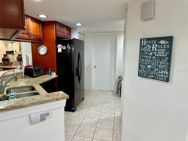 kitchen featuring light stone counters, light tile patterned flooring, black fridge with ice dispenser, and sink