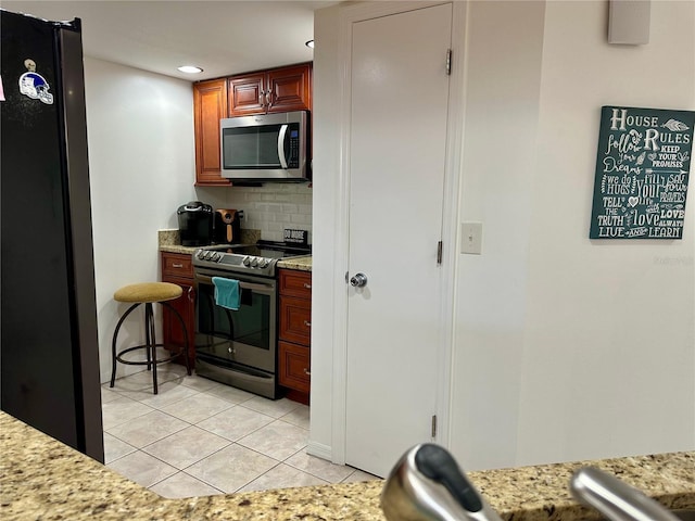 kitchen featuring backsplash, light tile patterned flooring, light stone counters, and stainless steel appliances