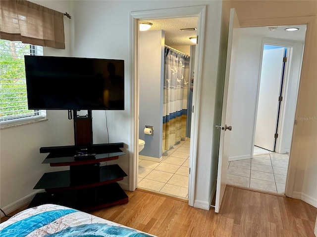 bedroom with ensuite bathroom, light hardwood / wood-style flooring, and a textured ceiling