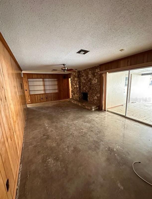 unfurnished living room with a textured ceiling, ceiling fan, concrete floors, and wood walls