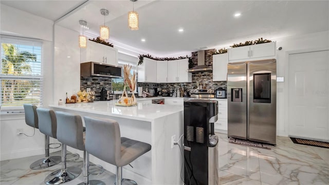 kitchen featuring white cabinets, wall chimney exhaust hood, pendant lighting, and stainless steel appliances