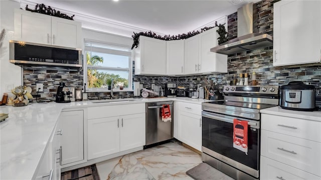 kitchen featuring white cabinets, appliances with stainless steel finishes, decorative backsplash, and wall chimney range hood