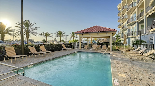 pool at dusk featuring a gazebo and a patio area