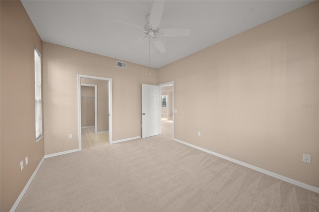 unfurnished bedroom with ceiling fan, light colored carpet, a walk in closet, and a closet