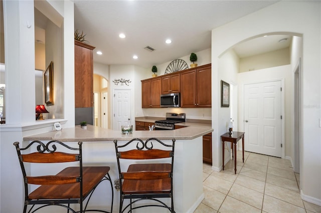 kitchen with a breakfast bar, kitchen peninsula, stainless steel appliances, and light tile patterned floors