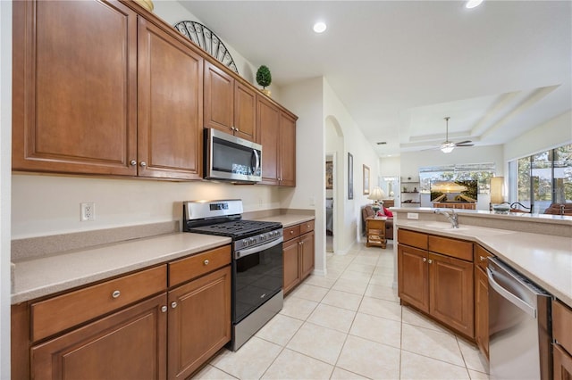 kitchen with ceiling fan, a raised ceiling, light tile patterned floors, and appliances with stainless steel finishes