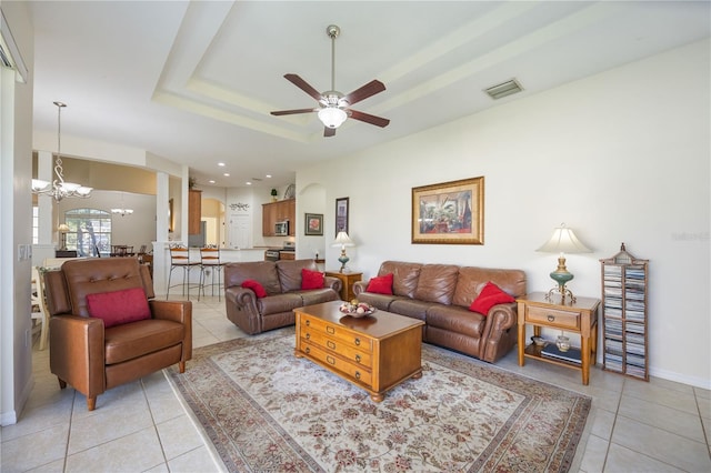 living room featuring a raised ceiling, light tile patterned floors, and ceiling fan with notable chandelier