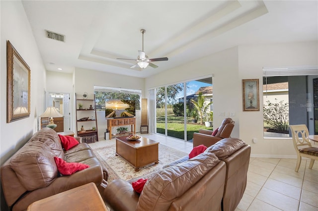 tiled living room with ceiling fan and a tray ceiling