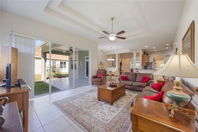 living room with a raised ceiling, light tile patterned flooring, and ceiling fan with notable chandelier