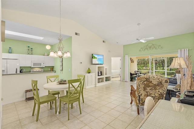 dining room with light tile patterned floors, ceiling fan with notable chandelier, and vaulted ceiling with skylight