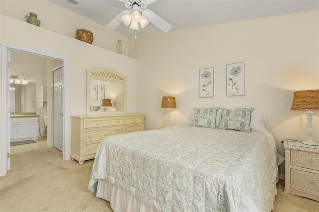 bedroom with ceiling fan, light colored carpet, and connected bathroom