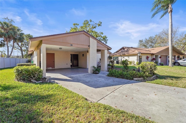 view of front of house with concrete driveway, an attached carport, fence, a front lawn, and stucco siding