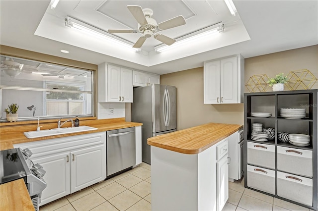 kitchen featuring light tile patterned floors, a sink, white cabinets, appliances with stainless steel finishes, and a tray ceiling