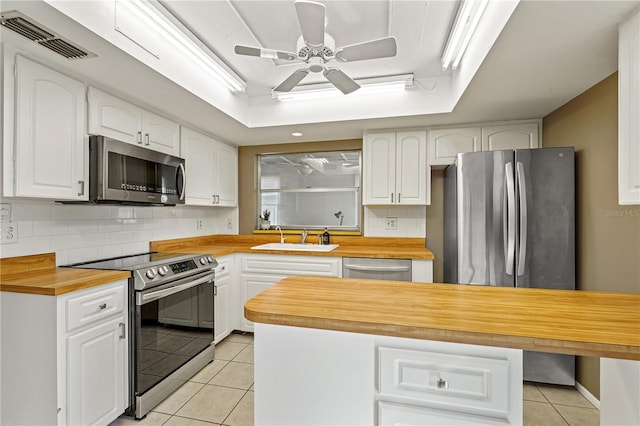 kitchen with stainless steel appliances, a tray ceiling, butcher block counters, and visible vents