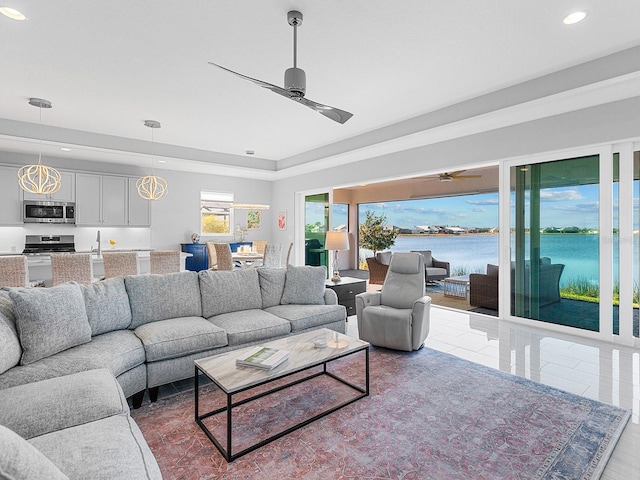 living room featuring a tray ceiling, ceiling fan, and a water view