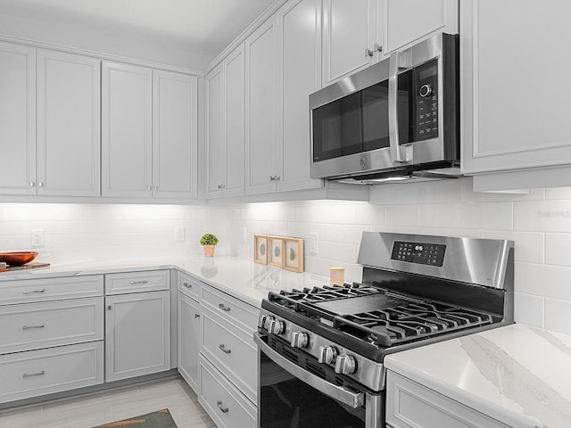 kitchen featuring white cabinets, decorative backsplash, light stone countertops, and appliances with stainless steel finishes