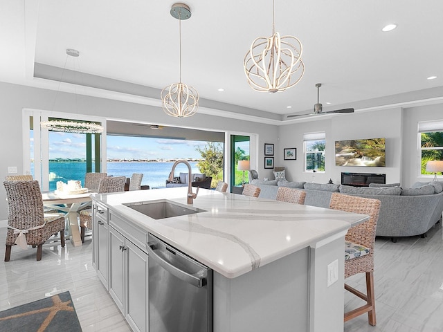 kitchen featuring light stone counters, a raised ceiling, sink, dishwasher, and an island with sink