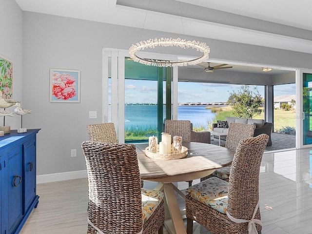 dining room featuring ceiling fan with notable chandelier and a water view