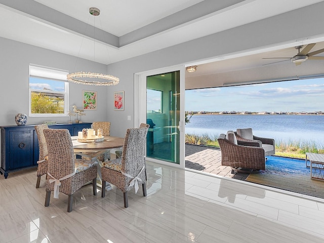 dining space featuring a raised ceiling, a water view, and ceiling fan with notable chandelier