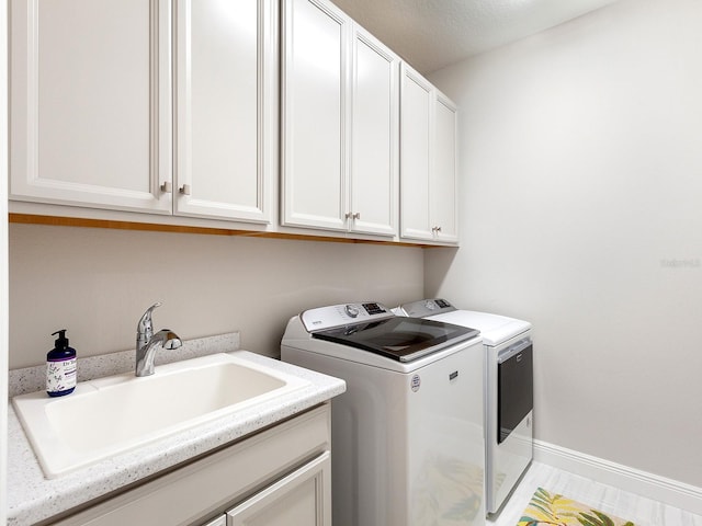 clothes washing area with washer and dryer, cabinets, and sink