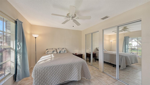 tiled bedroom featuring a textured ceiling, two closets, and ceiling fan