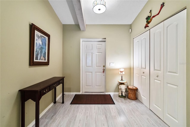 entryway with beam ceiling, light hardwood / wood-style flooring, and a textured ceiling