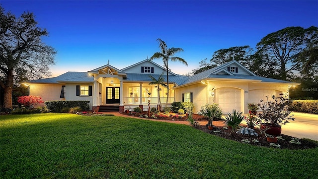 view of front of property with stucco siding, covered porch, an attached garage, metal roof, and a front lawn