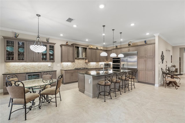 kitchen with wall chimney exhaust hood, stainless steel appliances, hanging light fixtures, and dark stone counters