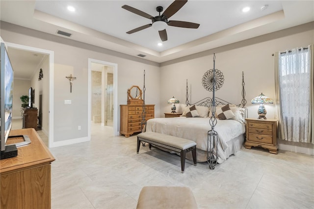 bedroom featuring a tray ceiling, ensuite bath, and ceiling fan