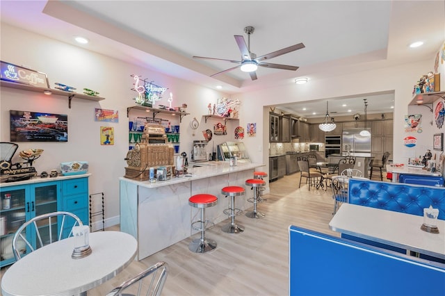 kitchen featuring a breakfast bar, decorative light fixtures, a tray ceiling, kitchen peninsula, and built in fridge