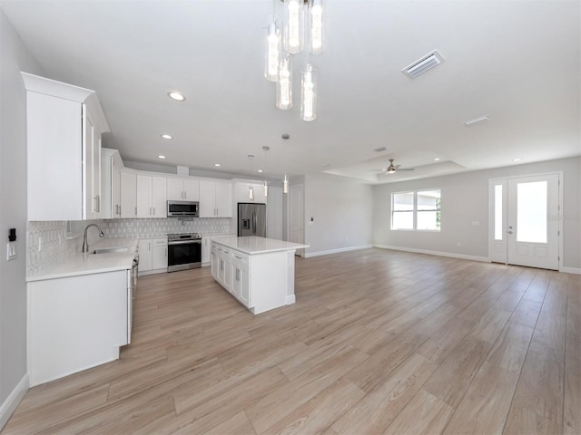 kitchen featuring a center island, hanging light fixtures, light wood-type flooring, appliances with stainless steel finishes, and white cabinetry