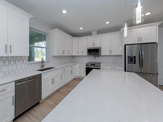 kitchen with appliances with stainless steel finishes, white cabinetry, hanging light fixtures, and sink