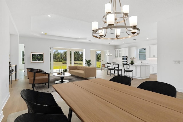 dining space with a raised ceiling, a notable chandelier, and light wood-type flooring