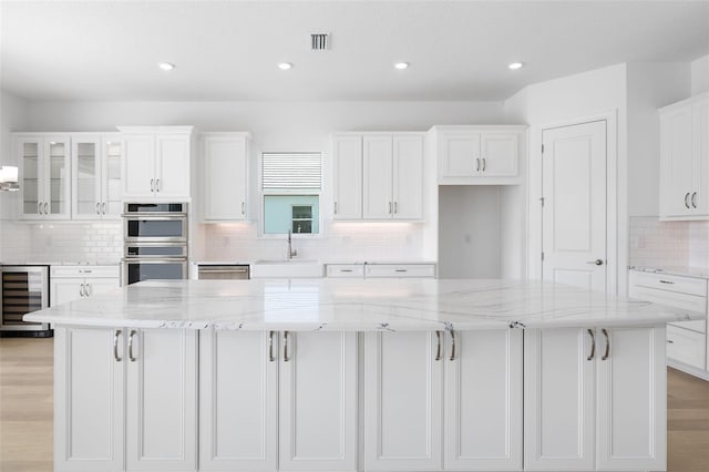 kitchen featuring white cabinetry, beverage cooler, light stone counters, double oven, and a spacious island