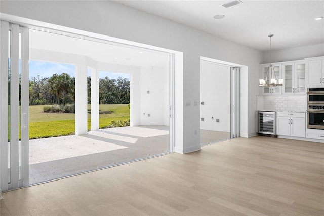 unfurnished living room with an inviting chandelier, beverage cooler, and light hardwood / wood-style flooring