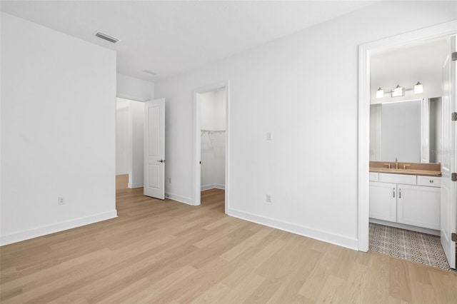 unfurnished bedroom featuring sink, light hardwood / wood-style flooring, and ensuite bath