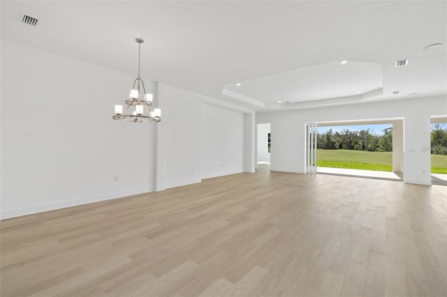 unfurnished living room with a notable chandelier, a raised ceiling, and light wood-type flooring