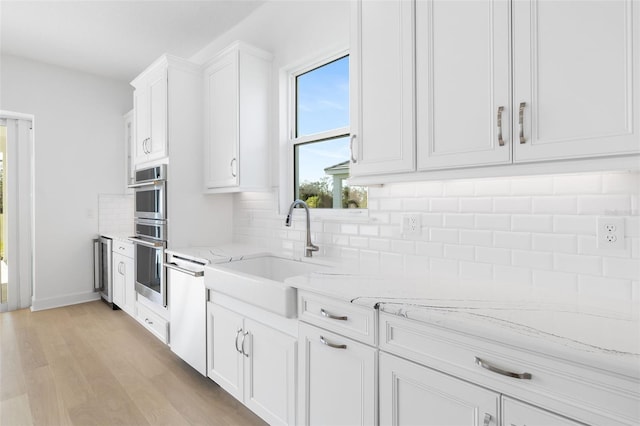 kitchen with sink, tasteful backsplash, light stone counters, light hardwood / wood-style flooring, and white cabinets