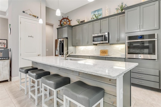 kitchen with gray cabinets, a kitchen island with sink, sink, and appliances with stainless steel finishes