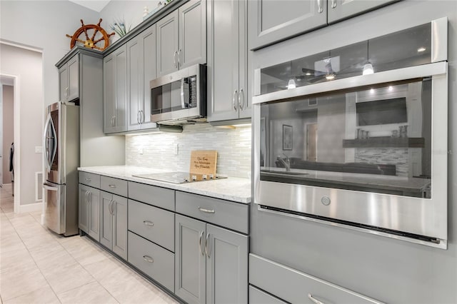 kitchen with decorative backsplash, appliances with stainless steel finishes, light stone counters, light tile patterned floors, and gray cabinets