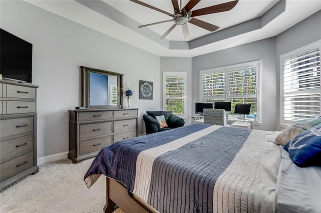 bedroom with ceiling fan, light colored carpet, and a tray ceiling