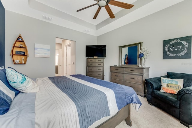 bedroom with ceiling fan, a raised ceiling, light carpet, and ensuite bath