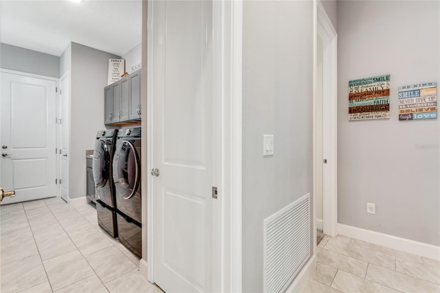 clothes washing area with cabinets, washing machine and dryer, and light tile patterned floors