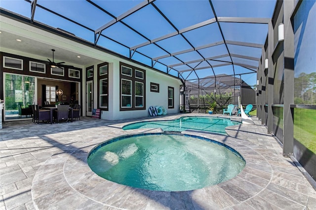 view of pool featuring glass enclosure, an in ground hot tub, a patio area, and ceiling fan