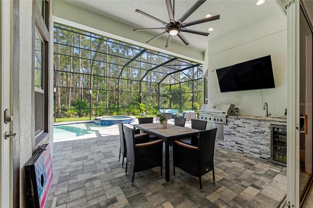 view of patio / terrace featuring glass enclosure, grilling area, ceiling fan, a swimming pool with hot tub, and exterior kitchen