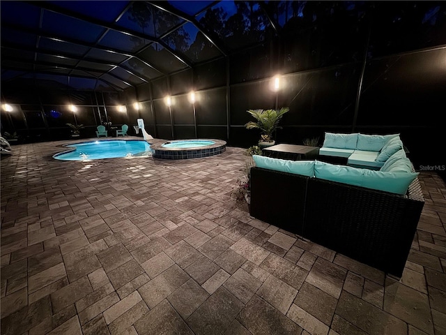 pool at night with an in ground hot tub, an outdoor living space, a patio, and a lanai