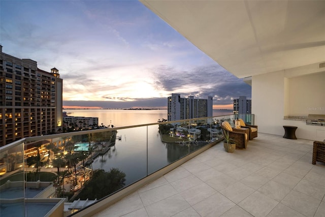 balcony at dusk featuring a water view